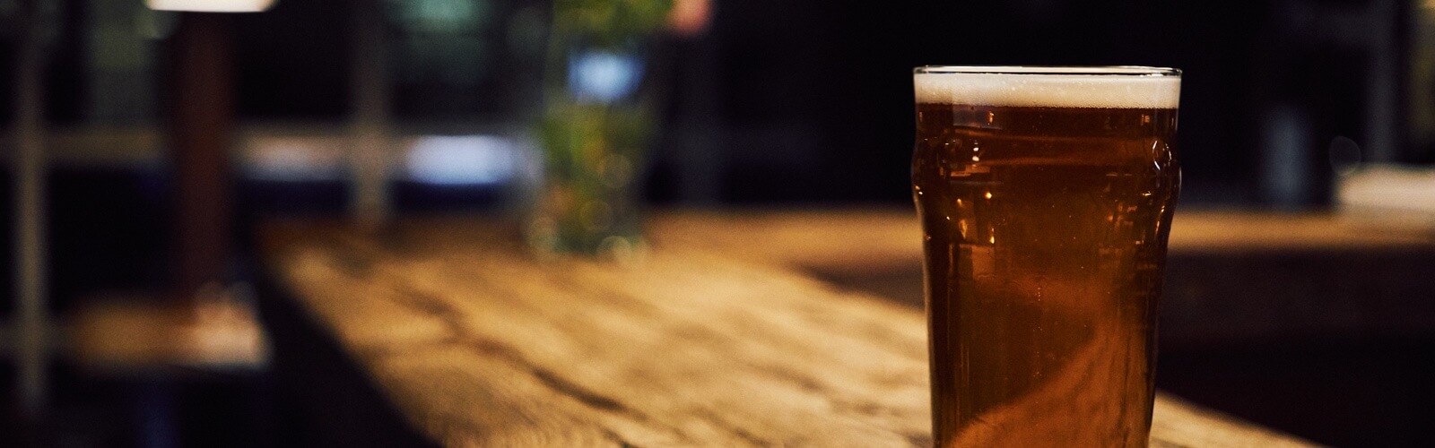 A pint of beer placed on the end of a wooden bar top