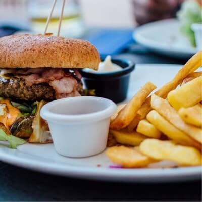 A burger and fries on a white plate with two dip containers in between them, one black and the other white.