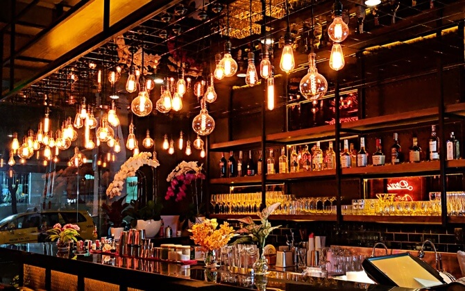 A fancy bar with many hanging incandescent bulbs providing the bar with an orange hue.