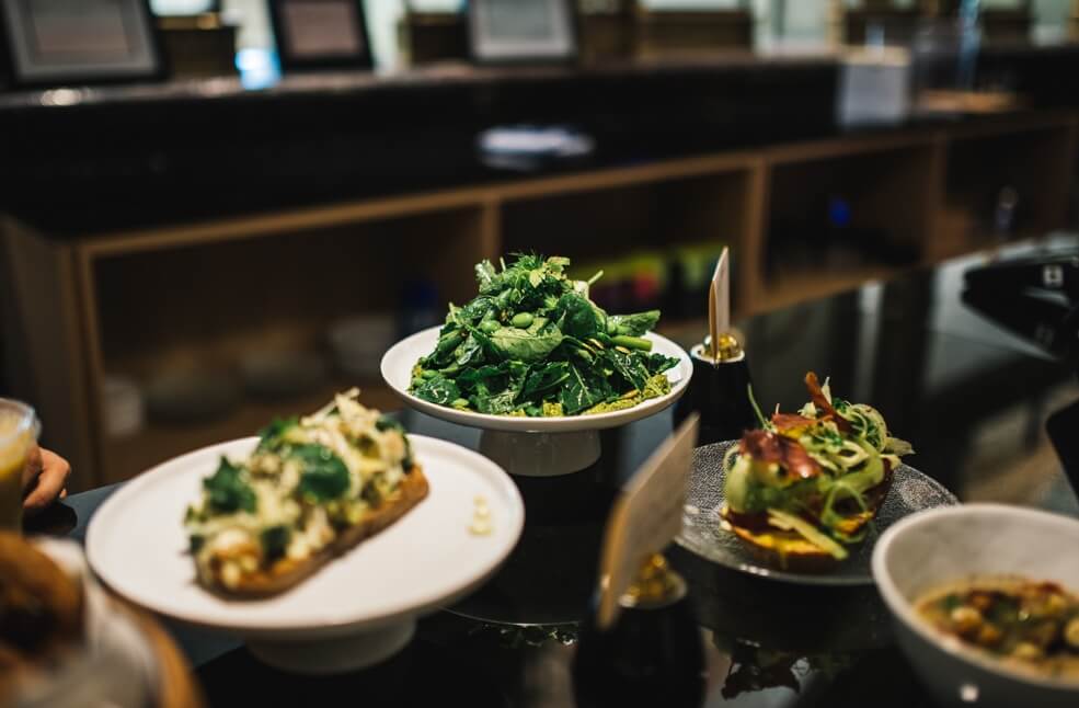 4 meals set on a shiny black table. A tall green salad is in focus at the center of the image