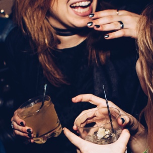 Two people laughing while holding drinks in their hands